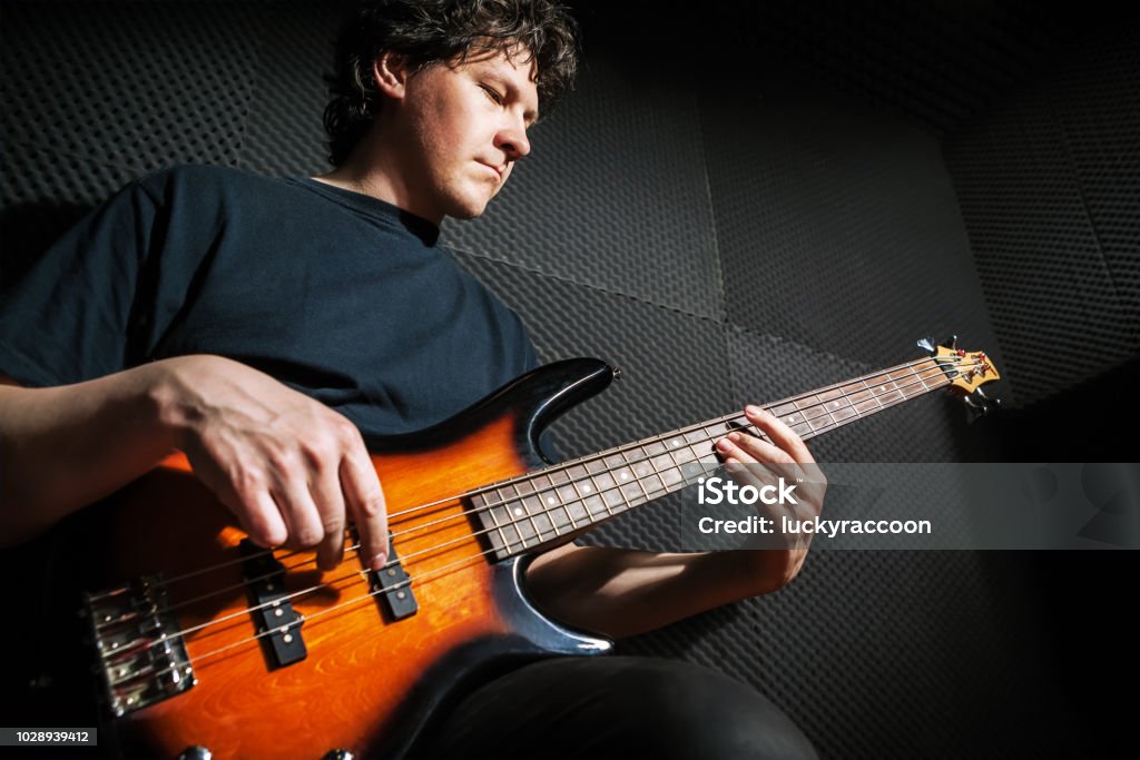 Handsome rock bass guitarist practicing. Handsome rock bass guitarist practicing in sound studio. Bass Guitar Stock Photo