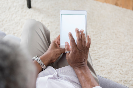 Senior African American man uses digital tablet at home. The device screen is blank.