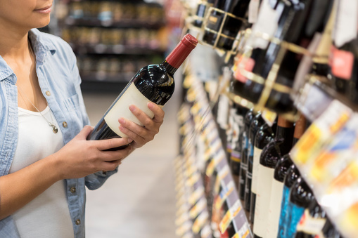 Mid adult woman reads label on bottle of red wine in grocery store.