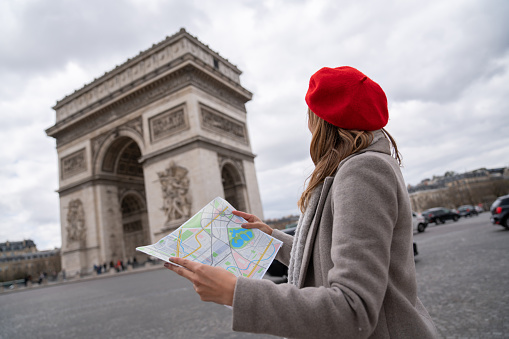 Happy female tourist with a map in Paris near the Arc de Triomphe - people traveling concepts. **DESIGN ON MAP WAS MADE FROM SCRATCH BY US**