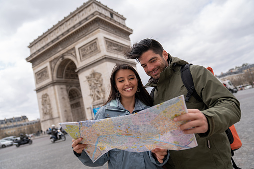 Happy couple of tourist sightseeing with a map in Paris near the Arc de Triomphe and smiling - people traveling concepts. **DESIGN ON MAP WAS MADE BY US FROM SCRATCH**