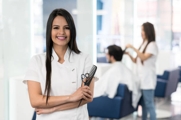 istock Professional hairstylist with arms crossed holding a comb and scissors while looking at camera smiling 1029002948