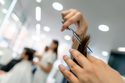 Close up of unrecognizable woman cutting a customers hair - focus on foreground