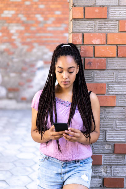 レンガの壁に戻って傾いているアフリカの女性 - braids african descent women pensive ストックフォトと画像