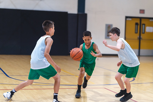 A young African American boy dribbles through two defenders and tries to score.