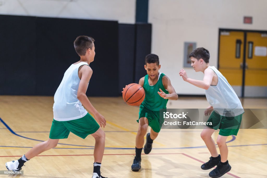 Elementary boys playing basketball A young African American boy dribbles through two defenders and tries to score. Basketball - Sport Stock Photo