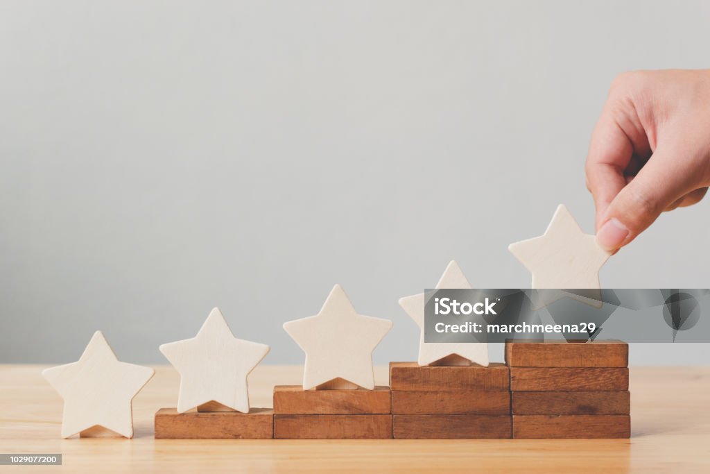 Mettendo a mano la forma a cinque stelle in legno sul tavolo. Il miglior eccellente concetto di customer experience di valutazione dei servizi aziendali - Foto stock royalty-free di Qualità