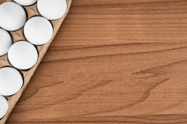istock Cardboard egg box disposed by diagonal on wooden table, top view. 1029079320