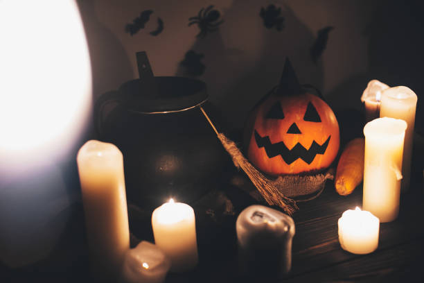 jack o lantern pumpkin with candles, bowl, witch broom and bats, ghosts on background in dark spooky room. Happy Halloween concept. fall halloween image