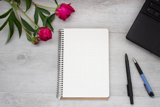 istock Open blank notepad, pen, peony and laptop on the light wooden table. Workplace flat lay 1029155260