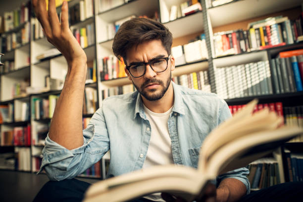 istock Cute hipster boy sitting on a library floor and looking through some books with curious face. 1029194028