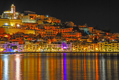 The vibrant Ibiza town lights up the waters of the port. The ancient fortifications and cathedral dominating the skyline.
