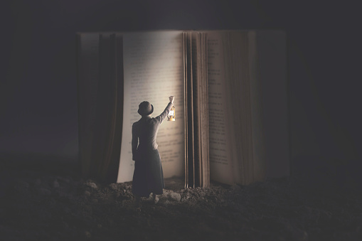 Curious woman illuminates with a lantern a giant book at night