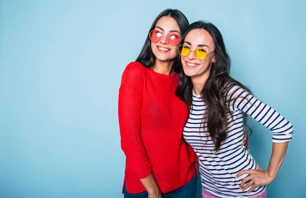 istock Two beautiful brunette women in sunglasses posing and hugging over blue background 1029231306