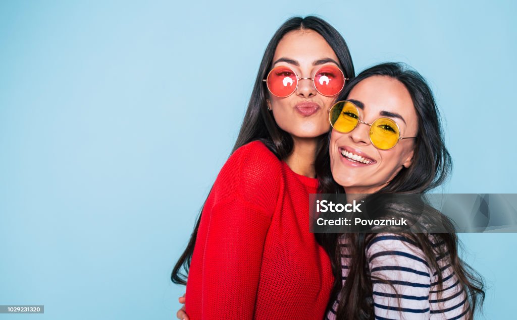 Friends forever. Two cute lovely girl friends in sunglasses posing with smile on blue background Friendship Stock Photo