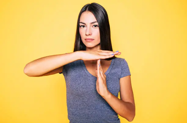 Stop and think. Portrait of young confident beautiful woman in casual wear is doing T symbol or sign with help of her hands and looks on camera