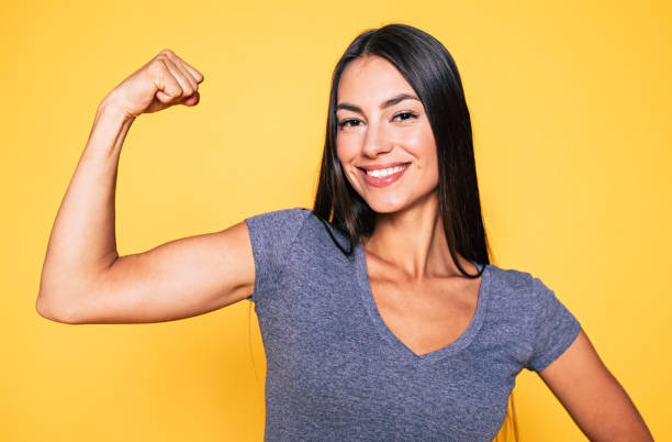 close up portrait of young cute sporty smiling brunette woman while she shows her arms and biceps on camera - flexing muscles fotos imagens e fotografias de stock