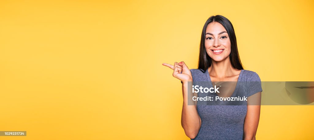 Photo of young excited beautiful happy brunette woman, girl pointing away and smile isolated on yellow background banner Women Stock Photo