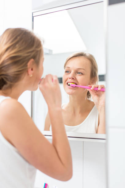 istock Pretty female brushing her teeth in front of mirror 1029240092