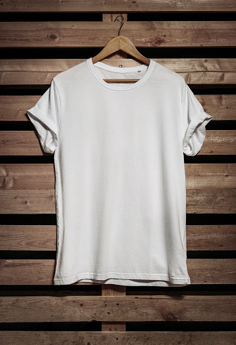 Blank white t-shirt hanging over wooden background with copy space