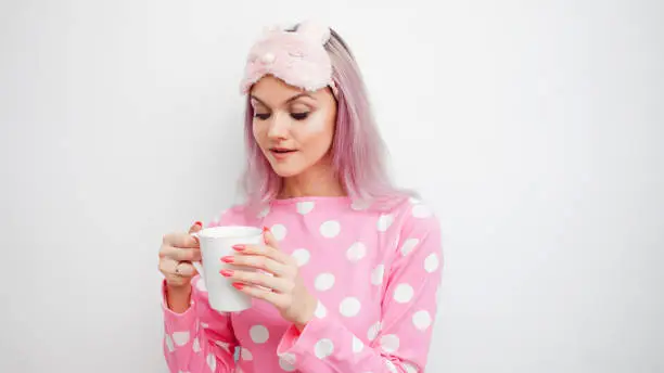 Happy young woman drink morning coffee. Beautiful girl in pink pajamas and mask for sleep