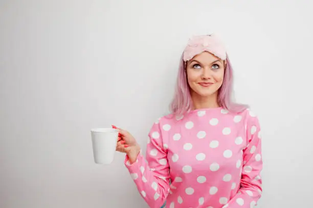 Happy young woman drink morning coffee. Beautiful girl in pink pajamas and mask for sleep