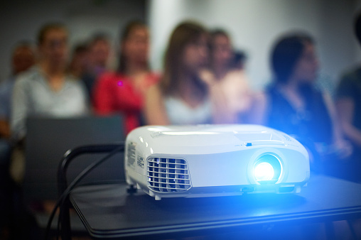 Close-up multimedia projector with blurred people background. Unrecognazible people.