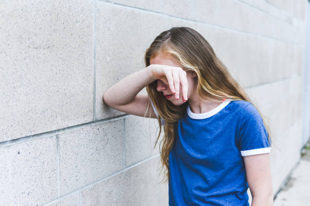 Sad teenage girl leaning against a brick wall. stock photo