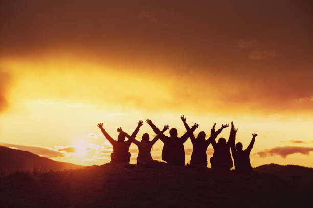 Happy friends with raised arms sunset silhouettes Silhouettes of happy friends with raised arms against sunset mountains group mountain silhouette stock pictures, royalty-free photos & images