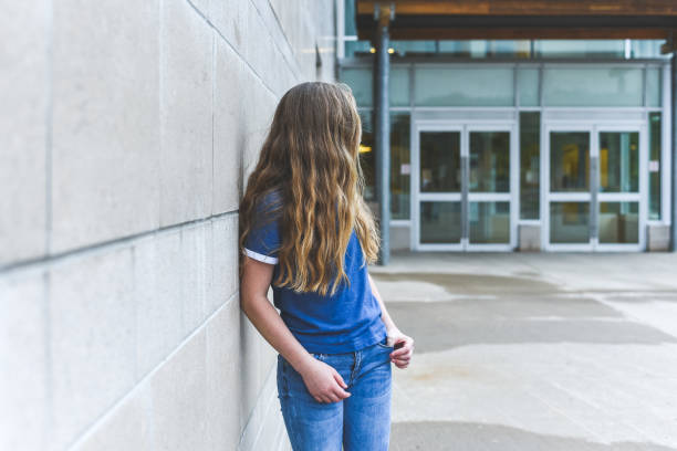niña adolescente mirando sobre su hombro mientras que se inclina contra una pared de ladrillos. - photography teenagers only vertical teenager fotografías e imágenes de stock