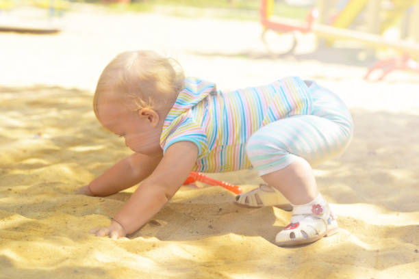 A little girl in striped clothes playing in a sandbox with sand. So develop fine motor skills and early thinking