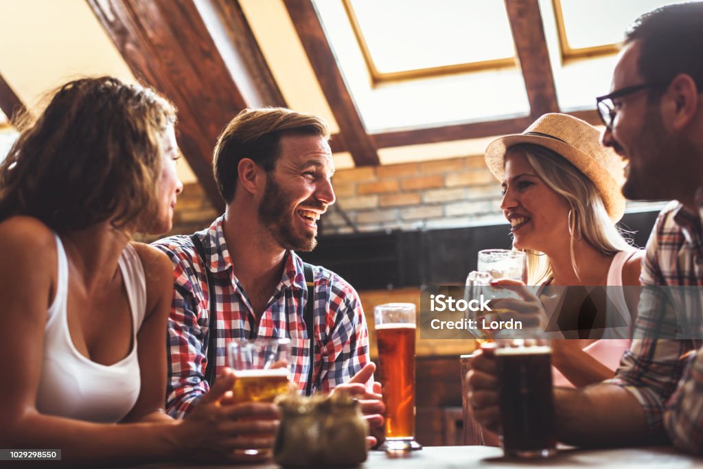 Young people drinking beer and laughing together Happy friends having fun at bar - Young trendy people drinking beer and laughing together Couple - Relationship Stock Photo