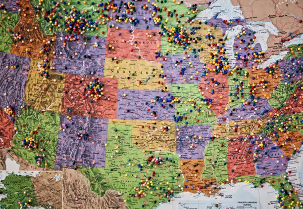 A paper map of the United States map hanging on a wall dotted with colorful pins marking destinations