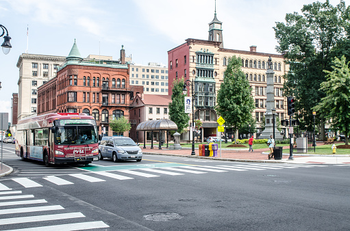 Corner of Court Street and Main Street in Springfield Massachusetts during summer day\nCar, bus and people are passing by.