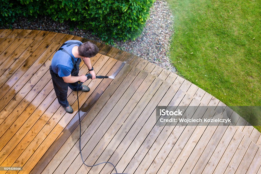 man cleaning terrace with a power washer - high water pressure cleaner on wooden terrace surface Yard - Grounds Stock Photo