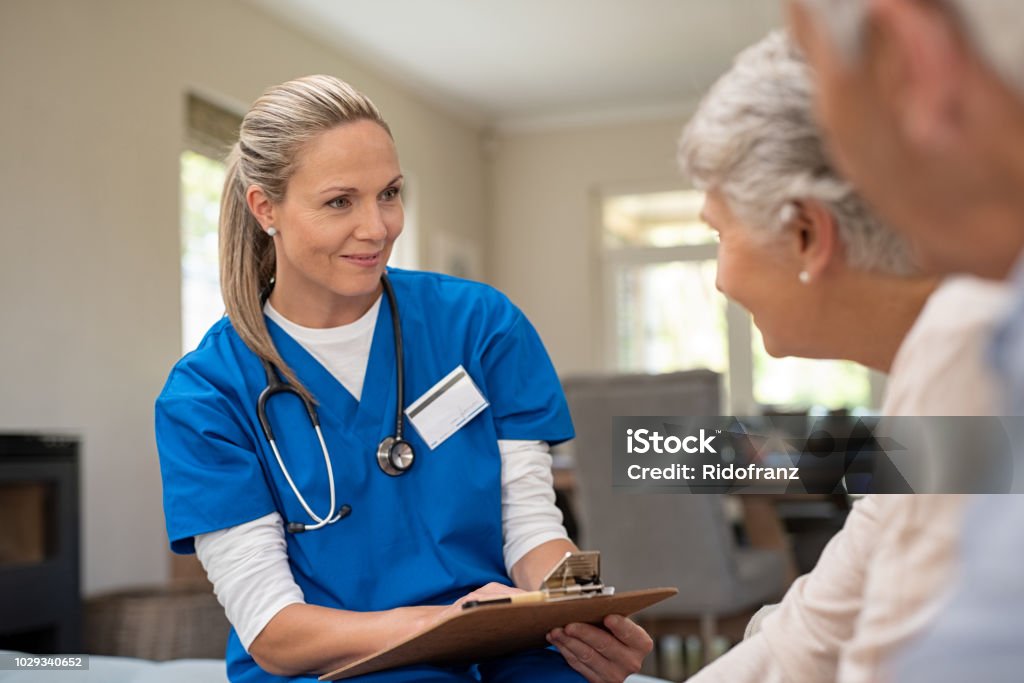 Friendly nurse talking with old couple Happy nurse talking to senior patients in private clinic. Senior couple consulting health and medical report with doctor at home. Old man and elderly woman visiting the nurse with clipboard and health issues. Nurse Stock Photo