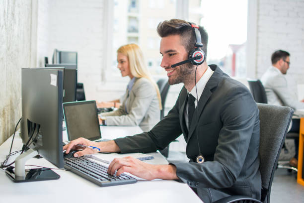 istock Portrait of a smiling young handsome man in formalwear with headset using computer in a office 1029340898