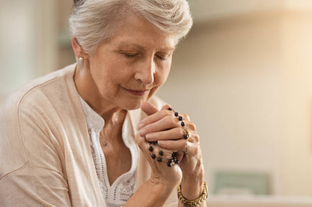 Senior woman praying Senior woman praying while holding christian symbol of crucifix. Old woman praying to god with hope and closed eyes. Elderly believer make a prayer with faith holding rosary in hands. rosary beads stock pictures, royalty-free photos & images