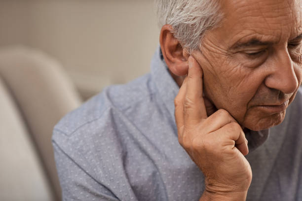 Senior man with hearing problems Side view of senior man with symptom of hearing loss. Mature man sitting on couch with fingers near ear suffering pain. deafness photos stock pictures, royalty-free photos & images