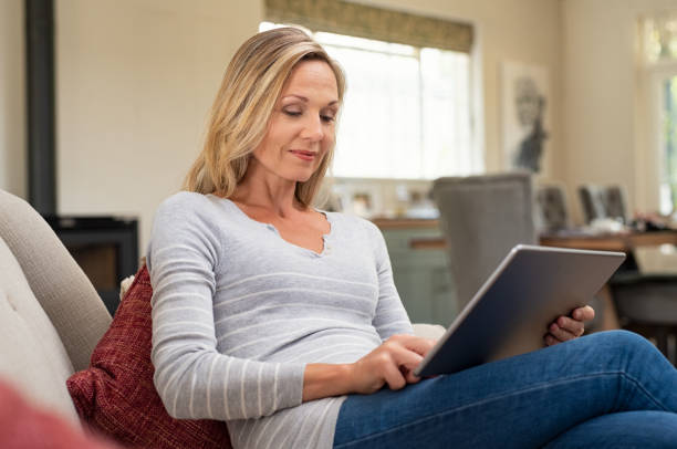 donna matura rilassante con tablet digitale - furniture internet adult blond hair foto e immagini stock