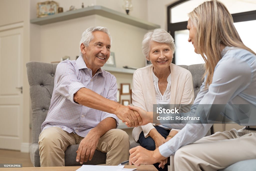 Senior couple shaking hands with financial advisor Happy senior couple sealing with handshake a contract for the retirement. Smiling satisfied retired man making sale purchase deal concluding with a handshake. Elderly man and woman smiling while agree with financial advisor. Senior Adult Stock Photo