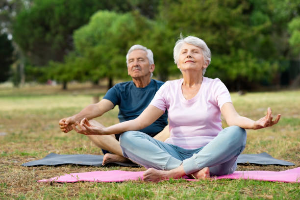 Senior couple doing yoga Old couple relaxing while sitting in lotus pose. Senior man and elderly woman meditating sitting in lotus position at park with closed eyes. Aged man and woman feeling relaxed sitting on yoga mat. peace park stock pictures, royalty-free photos & images
