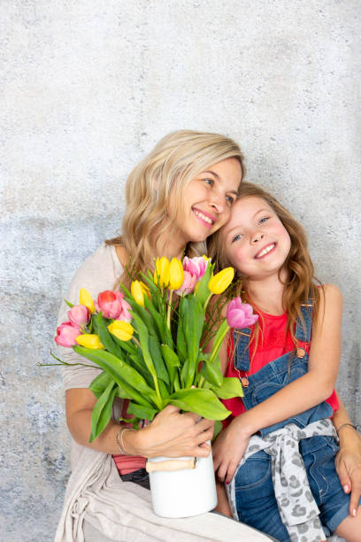istock Smiling Mother And Daughter With Bouquet Standing Against Wall 1029349968