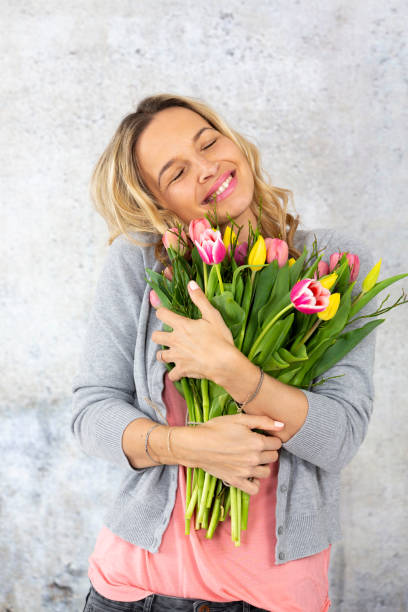 istock Smiling Woman Holding Flowers Against Wall 1029350464