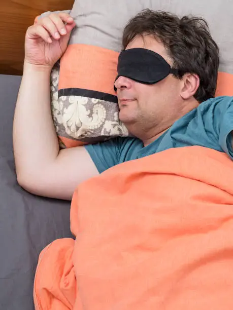 Photo of top view of mature man in black mask sleeps on bed