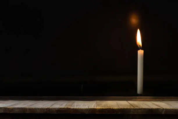 Photo of Wooden table in front of light candle burning brightly in the black background, can used for display or montage your products.