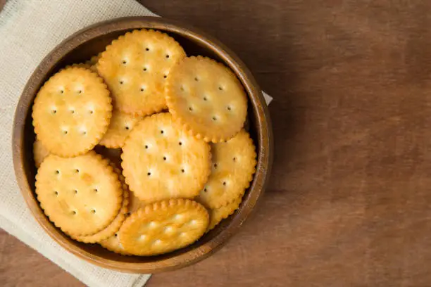 Photo of Round salted cracker cookies in wooden bowl putting on linen and wooden background