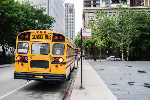 A school bus parked in a street, waiting the end of the class with the front door open, in dull weather. Back view, USA.