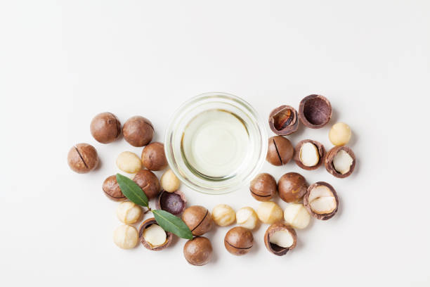 istock Cosmetic macadamia oil and heap of nuts on white table from above. 1029373312