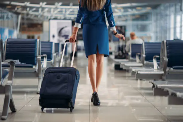 Air hostess with suitcase going between seat rows in airport. Stewardess with baggage, flight attendant with hand luggage, aviatransportations job